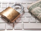 A padlock and dollar bills rest on a computer keyboard.