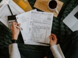Person reviewing documents with calculator and laptop.
