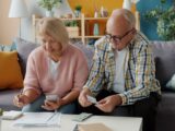 Elderly couple reviews finances at home on couch.