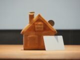 A small house bank with a coin and blank card.