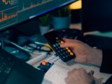 Person using calculator at desk with computer charts.