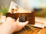 A person holding a small house and some money