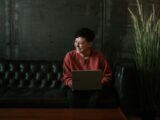 smiling man using laptop computer while sitting on black leather sofa
