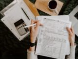 Person reviewing documents with calculator and laptop.