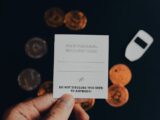 a person holding a business card in front of a pile of coins