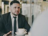 Man in suit talking across table with coffee.