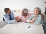 Senior couple in office meeting with consultant, discussing financial documents and smiling.