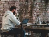 man in beige hoodie sitting on chair using laptop computer