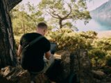 a man sitting on top of a rock next to a tree