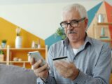 Elderly man using smartphone and credit card for online shopping.