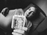 a man laying in bed holding a money bill
