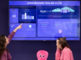 Two women look at a solar club dashboard display.