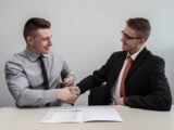 two men facing each other while shake hands and smiling