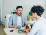 a man sitting at a table talking to a woman
