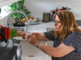 Woman filling a glass with water from a kitchen faucet