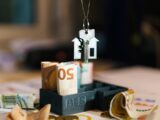 A house hanging from a string on top of a pile of money
