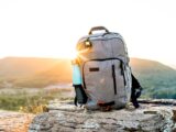 grey and black hiking backpack and cyan tumbler on grey rock during sunset