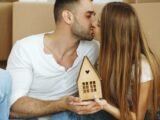 Couple kissing while holding a small wooden house.