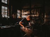 man holding hammer while forging on anvil inside room