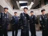 Five young men in matching black jackets stand together