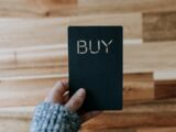 a person holding a black book with the word buy written on it