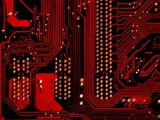 A red and black circuit board with intricate metallic pathways and solder points