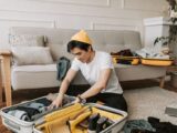 Young man organizing clothes in a suitcase in a cozy living room, preparing for travel.